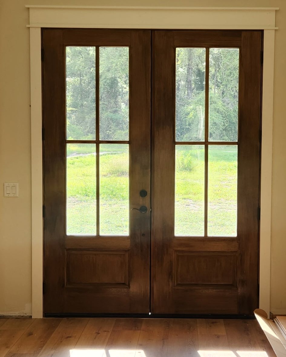 Walnut-stained 4-lite true divided light double entry doors installed in a Jacksonville home — Norwood Supply